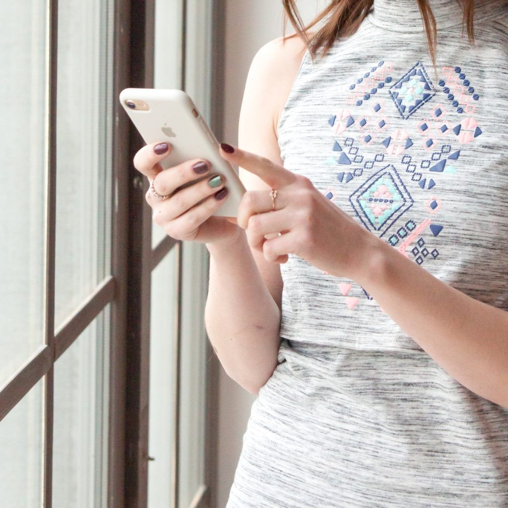 woman in gray and blue tank top holding white smartphone